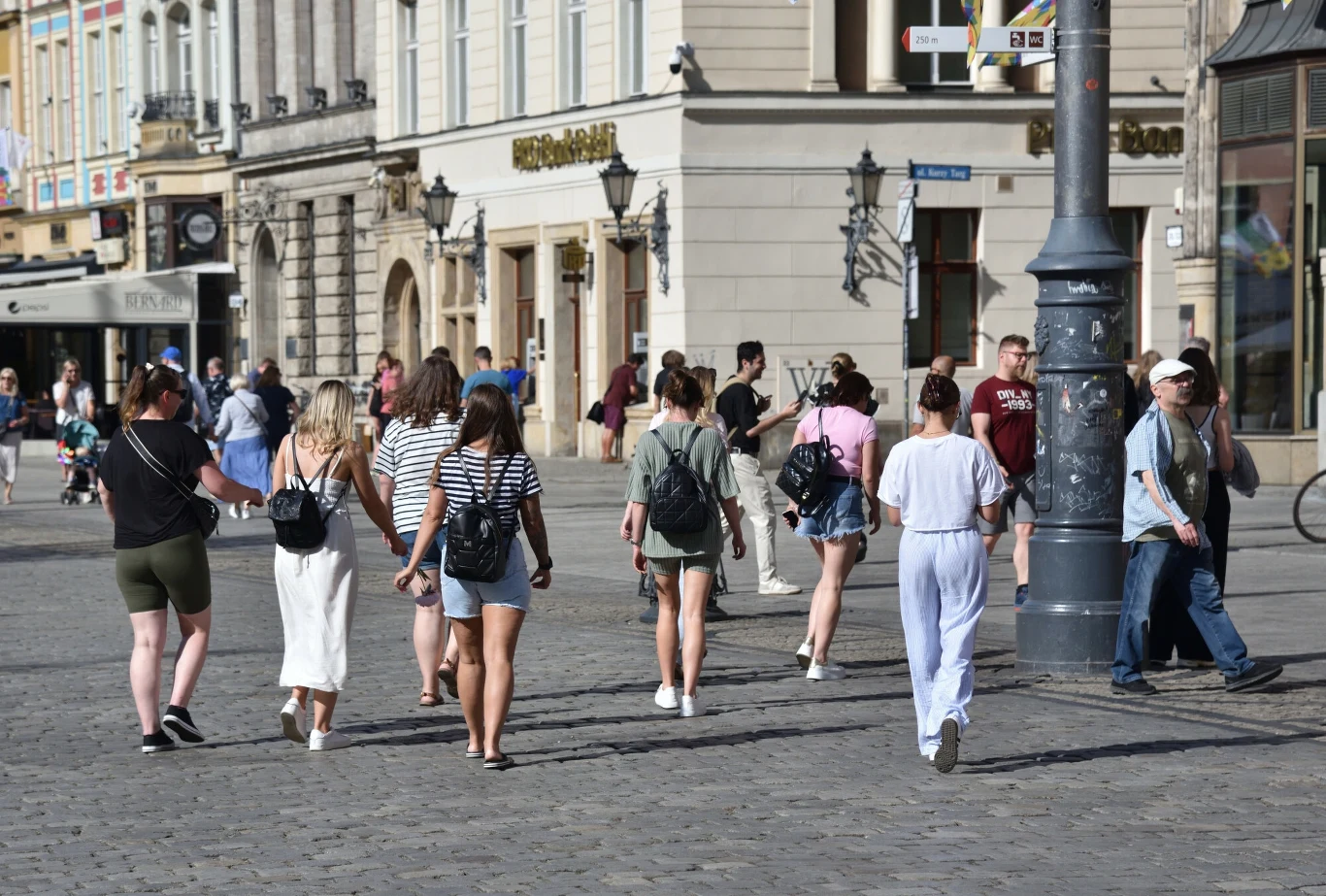 Stan demokracji w Polsce w 2024 r. miał ulec poprawie Grupa młodych osób spaceruje po brukowanej ulicy w centrum miasta w ciepły, słoneczny dzień; kobiety i mężczyźni ubrani są w letnie, codzienne stroje, mijają klasyczne kamienice i lokale, po stronie obserwatora widoczne są sylwetki przechodniów.
