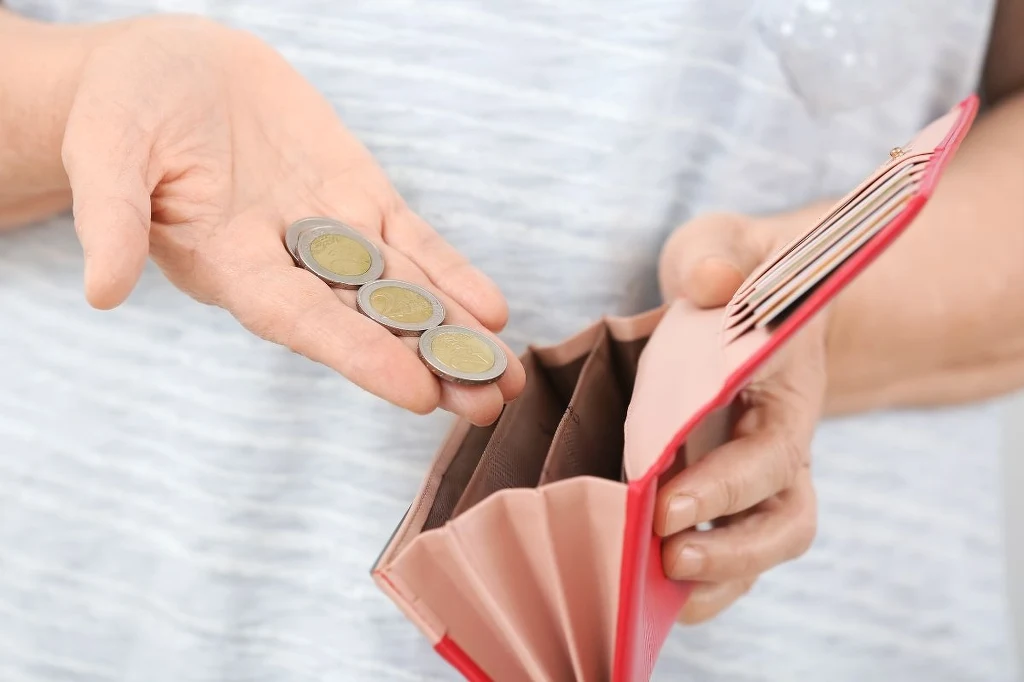 Stary, zniszczony portfel należy jak najszybciej wyrzucić Otwarte czerwone etui na portfel trzymane w jednej ręce, w drugiej dłoni umieszczone są cztery monety euro.