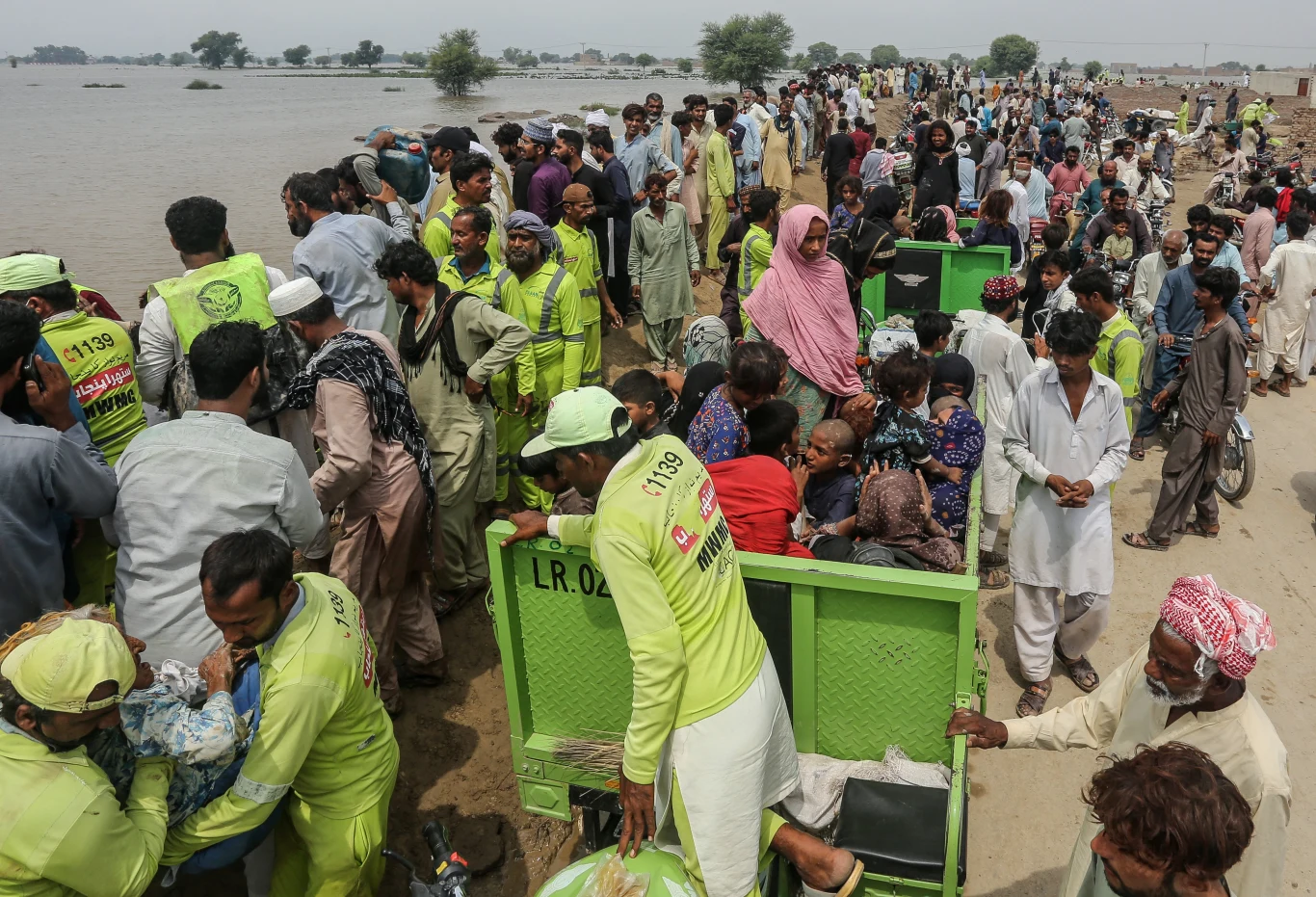 Powodzianie gromadzą się w bezpiecznym miejscu w Jalalpur Pirwala 8 września w pakistańskim stanie Pendżab, po tym jak rzeka Chenab wystąpiła z brzegów Tłum ludzi podczas akcji ratunkowej nad brzegiem zalanego terenu, ratownicy w odblaskowych uniformach pomagają w ewakuacji, w tle rozciąga się woda i widać zaniepokojone twarze rodzin czekających na pomoc.