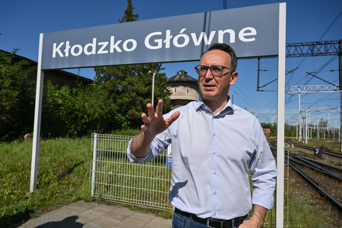 Minister infrastruktury Dariusz Klimczak podsumował działania na rzecz odbudowy gmin dolnośląskich po zeszłorocznej powodzi Mężczyzna w okularach i koszuli na peronie stacji kolejowej Kłodzko Główne, w tle widoczne tory oraz tablica informacyjna z nazwą stacji.