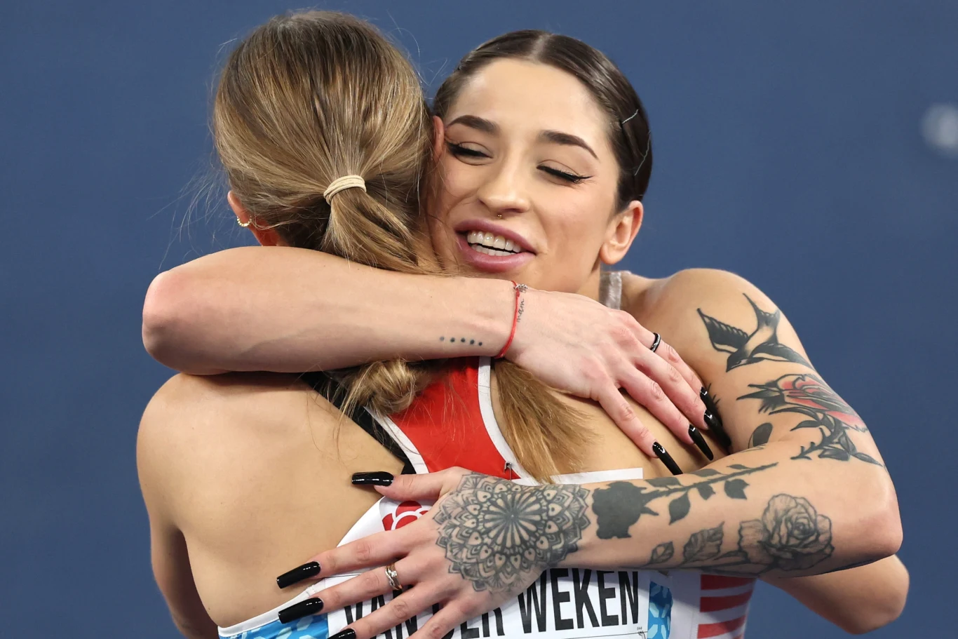Ewa Swoboda Dwie kobiety obejmują się po zakończonych zawodach sportowych, jedna z nich ma tatuaże na rękach, obie ubrane są w stroje sportowe, w tle niebieskie rozmazane tło.