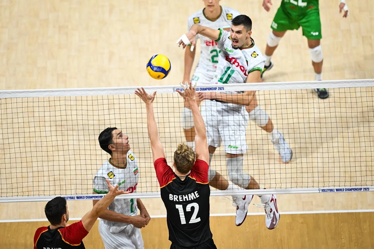 Aleks Grozdanow w reprezentacji Bułgarii Mecz siatkówki w trakcie dynamicznej akcji, jeden z zawodników ubrany w zielono-biały strój wykonuje atak przy siatce, zawodnik drużyny przeciwnej w czerwono-czarnym stroju próbuje blokować piłkę, w tle widoczni pozostali gracze.