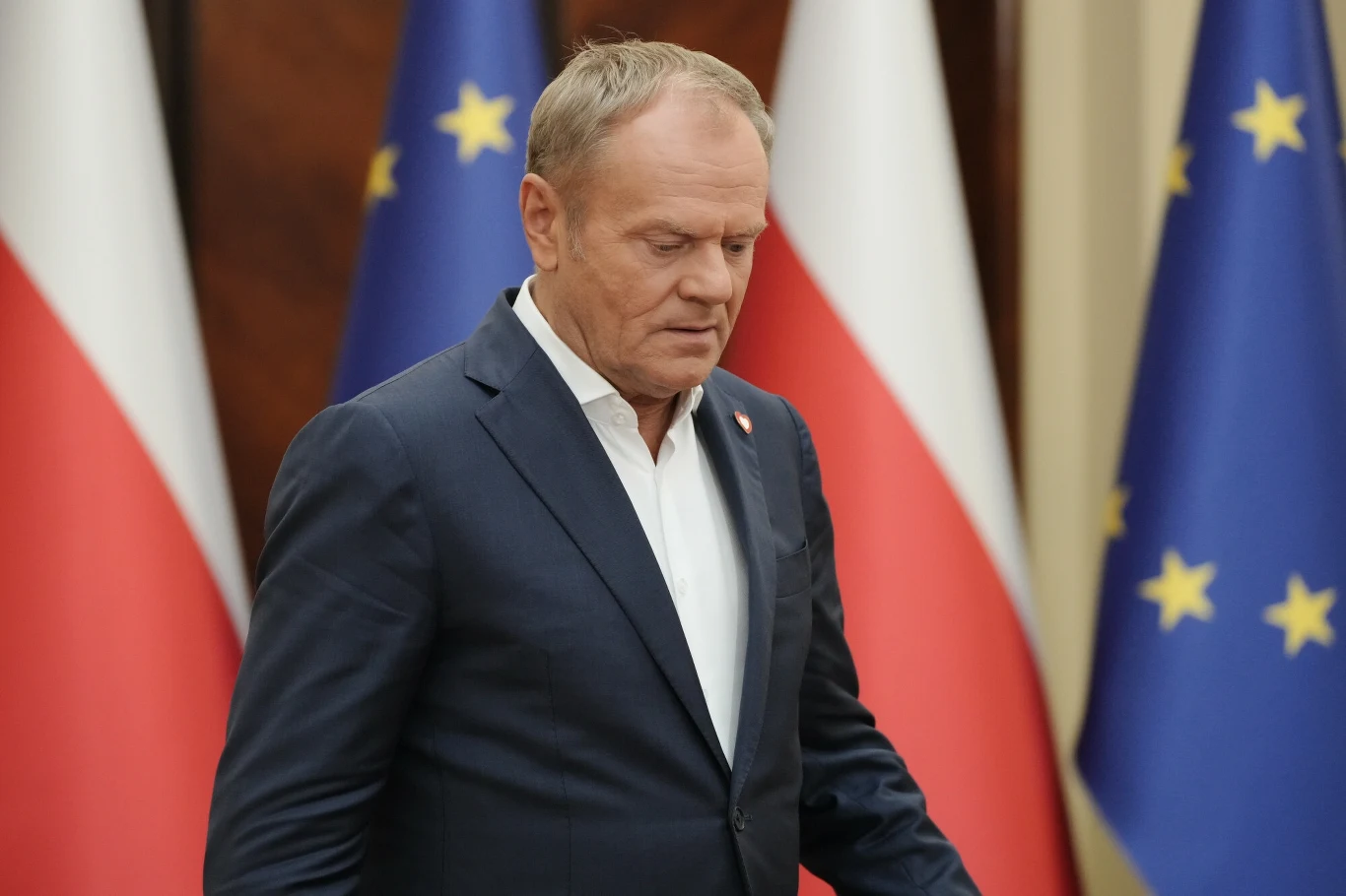 Donald Tusk reaguje na komentarze prawicy. W tle atak dronów Mężczyzna w garniturze na tle polskich i unijnych flag, w poważnym wyrazie twarzy, skierowany lekko w bok, w oficjalnym otoczeniu.