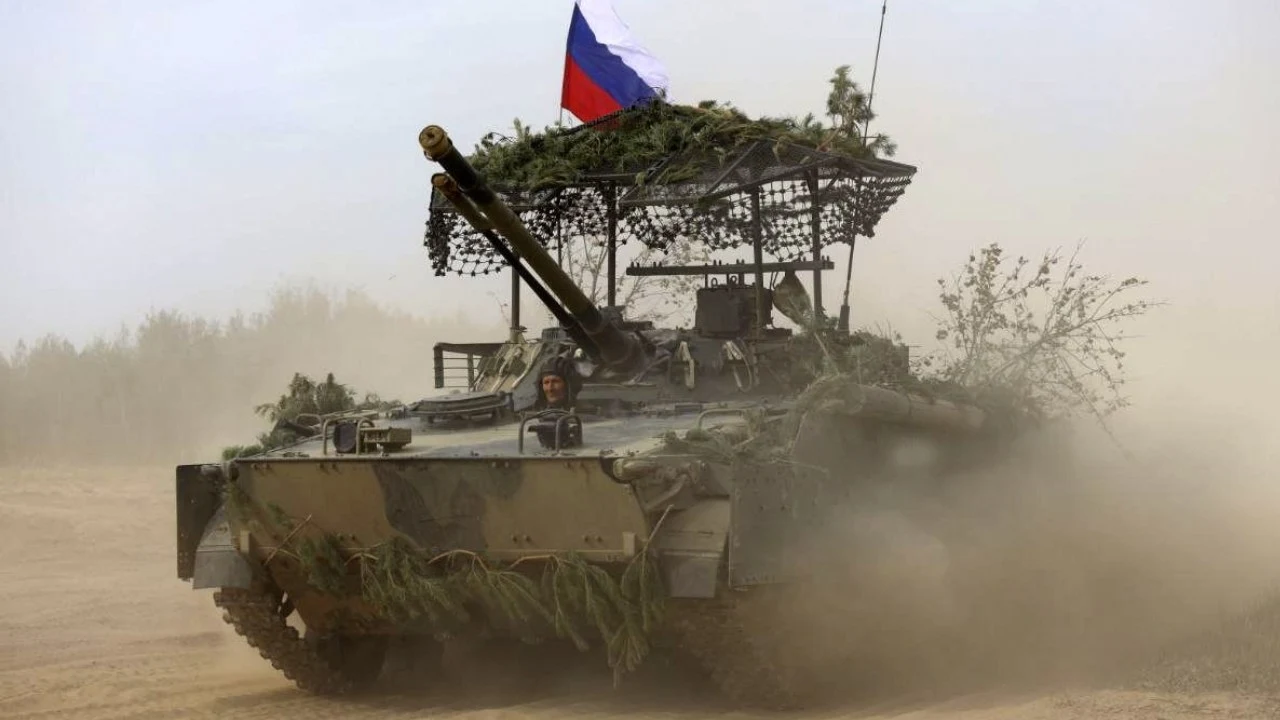 Od początku wojny ponad milion rosyjskich żołnierzy zostało zabitych, rannych lub zaginęło | Zdjęcie ilustracyjne Czołg opancerzony poruszający się wśród kurzu na poligonie, camuflowany gałęziami z rosyjską flagą na wieżyczce.