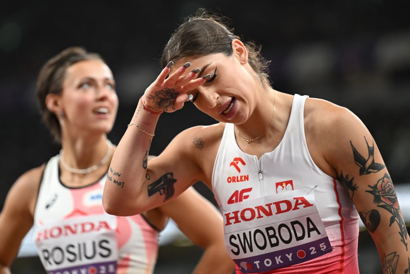 Dwie zawodniczki na bieżni, jedna z nich wykonuje gest zmęczenia lub rozczarowania, na strojach widoczne nazwiska oraz logotypy sponsorów.