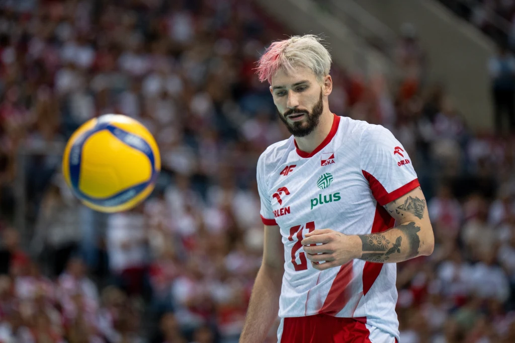 Tomasz Fornal Siatkarz w biało-czerwonym stroju z numerem 16 koncentruje się na piłce podczas meczu, a w tle widać trybuny wypełnione kibicami.