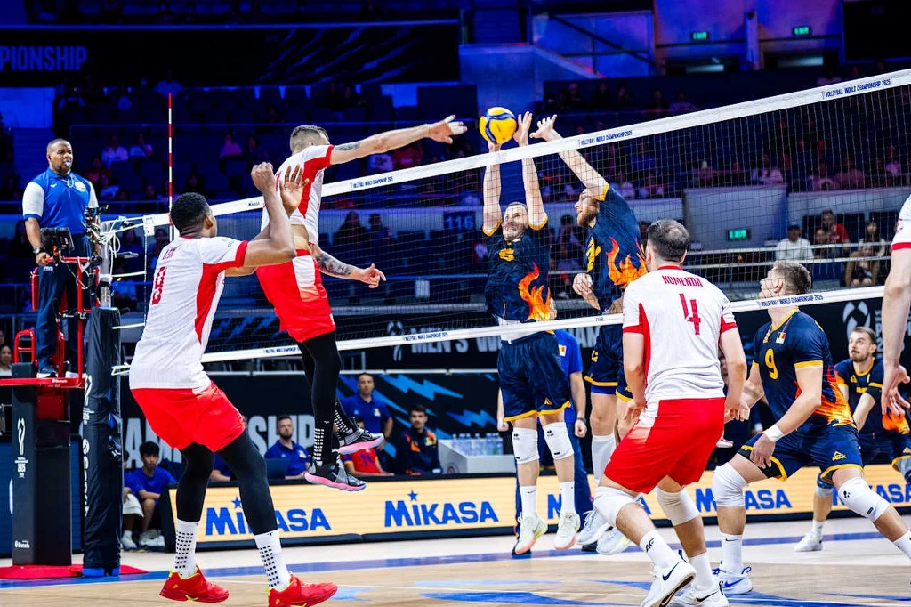 Norbert Huber w ataku Zawodnicy dwóch drużyn siatkarskich walczą o punkt przy siatce podczas meczu w hali sportowej, dynamiczna akcja w trakcie bloku ze strony jednej drużyny i ataku z drugiej, w tle sędzia, ławka rezerwowych oraz kibice.