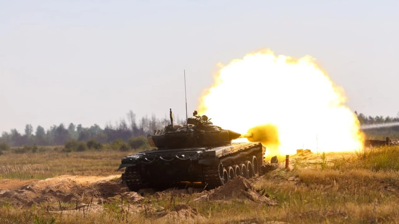 Zapad. Ekspert wojskowy o ukrytym celu manewrów Czołg na polu otwartym oddaje strzał, z lufy wydobywa się potężny błysk, wokół widać suchą trawę oraz odległą linię drzew na horyzoncie.
