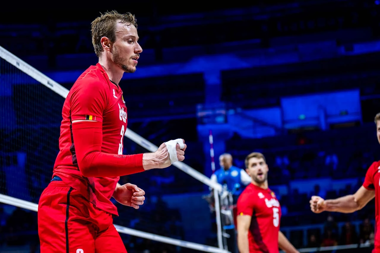 Siatkarz ubrany w czerwony strój drużynowy z numerem 9 świętuje punkt podczas meczu, w tle widoczni pozostali zawodnicy i fragment siatki na hali sportowej.