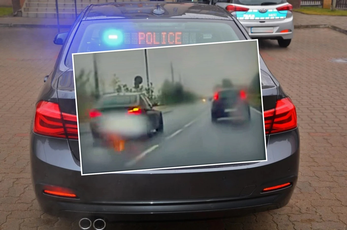 Nieoznakowany radiowóz wyprzedzał inny samochód przed przejściem dla pieszych Nieoznakowany radiowóz policyjny z włączonymi światłami i napisem POLICE na tablicy LED, na zbliżeniu ekran monitoringu pokazuje nagranie innego auta poruszającego się po drodze w deszczowych warunkach.