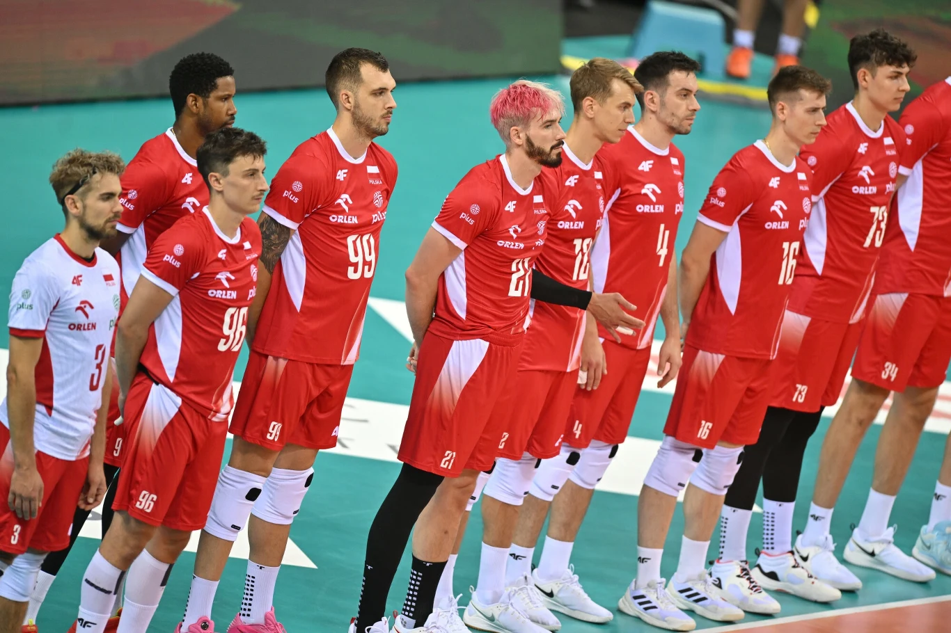 Jan Firlej wraca do zdrowia. Tomasz Fornal jest bliżej uporania się z dolegliwościami innej natury Zawodnicy męskiej reprezentacji Polski w siatkówce stoją w szeregu w czerwono-białych strojach sportowych na hali, skoncentrowani przed rozpoczęciem meczu.