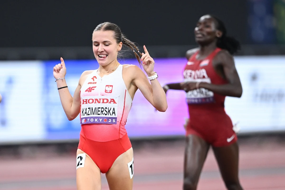 Polska lekkoatletka w biało-czerwonym stroju kończy bieg na stadionie, unosząc ręce w geście triumfu, za nią rywalka z Kenii również biegnie do mety.