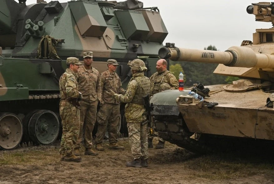 W przypadku ataku Rosji Polacy wierzą w pomoc sojuszników - wynika z nowego sondażu. Zdj. ilustracyjne Grupa żołnierzy w umundurowaniu stoi i rozmawia pomiędzy dwoma wojskowymi pojazdami opancerzonymi, w tym czołgiem, na tle ziemi i lekkiego zachmurzenia.