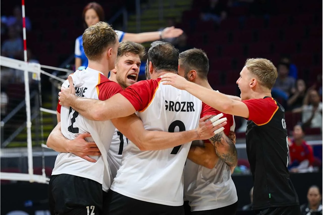 Siatkarze reprezentacji Niemiec Grupa zawodników drużyny siatkarskiej w biało-czarnych strojach z czerwonymi rękawami obejmuje się i cieszy z sukcesu podczas meczu, na ich twarzach widoczne są silne emocje i radość.