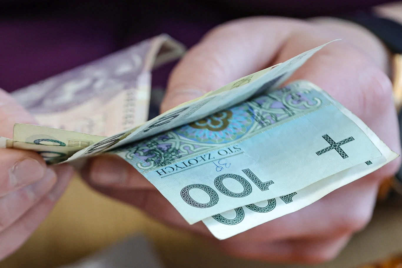 NBP podał nowe dane o inflacji bazowej Ręce osoby liczą banknoty o różnych nominałach, na pierwszym planie banknot stuzłotowy polski.