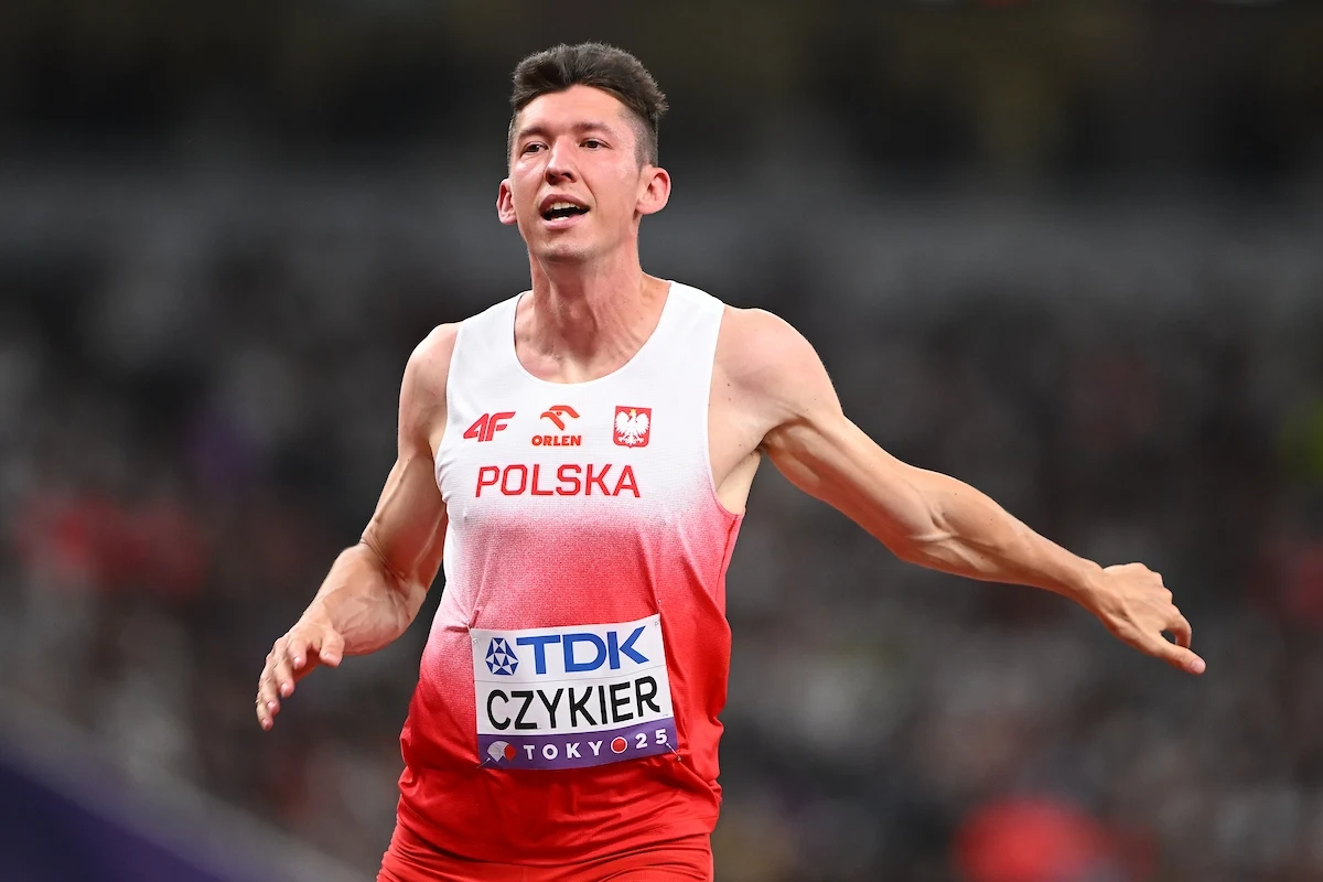 Lekkoatleta w stroju reprezentacji Polski podczas biegu, widoczne napięcie mięśni i skupienie twarzy, numer startowy oraz napis z nazwiskiem na piersi.