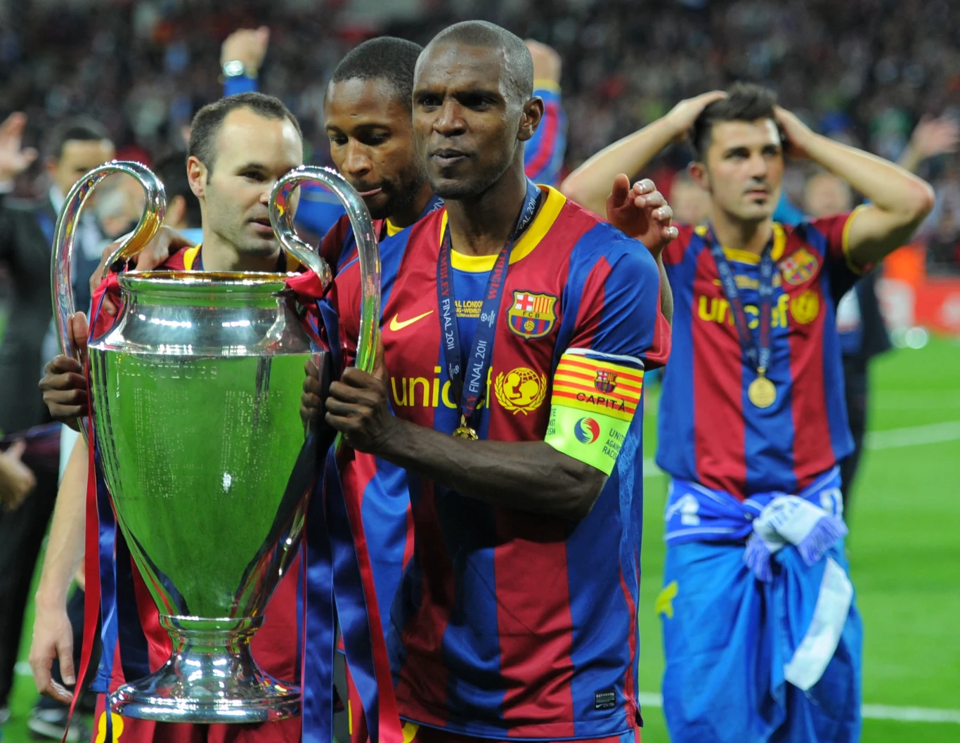 Eric Abidal z kapitańską opaską w barwach Barcelony... Piłkarze FC Barcelony świętują zdobycie trofeum Ligi Mistrzów UEFA na boisku, trzymając puchar, ubrani w klubowe koszulki w granatowo-bordowe pasy.