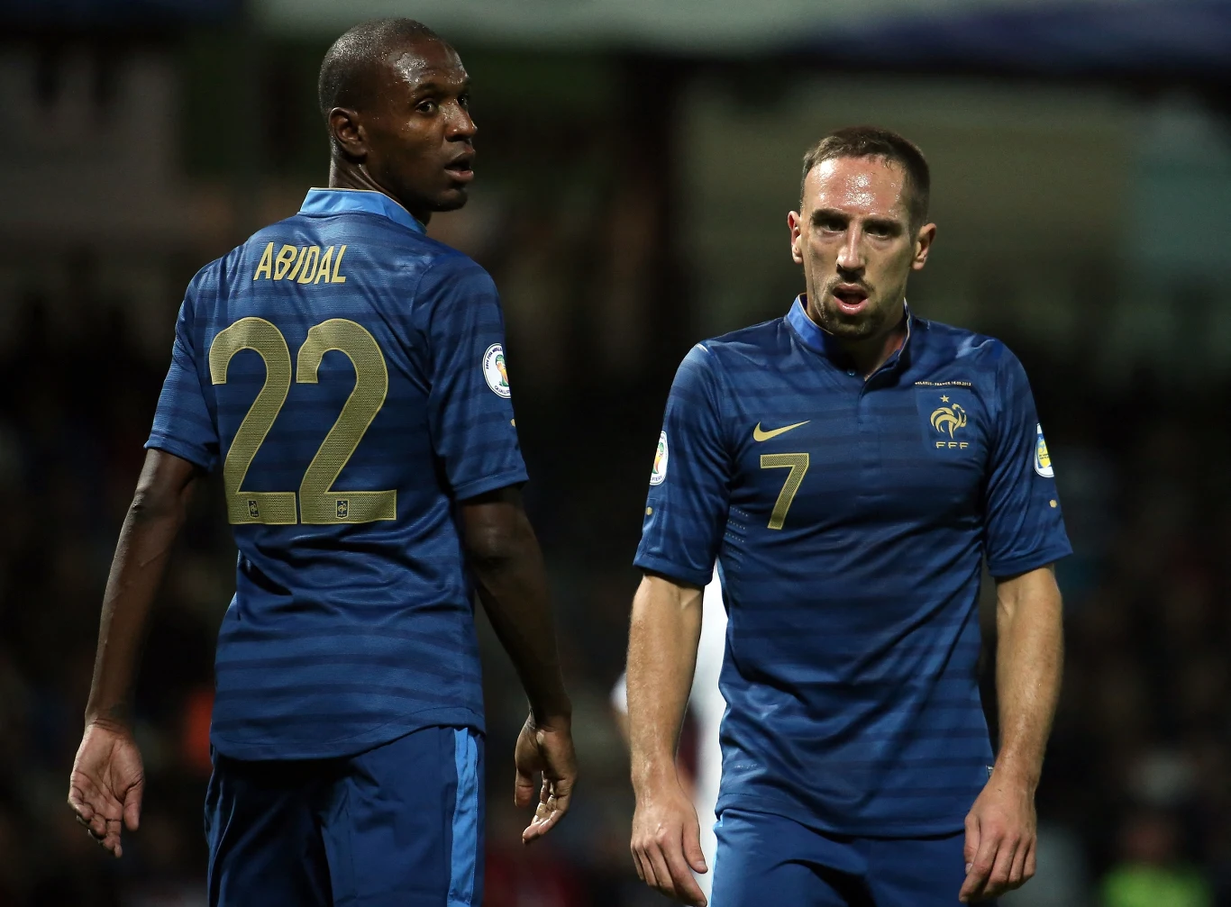 ...i jako reprezentant Francji (obok Franck Ribery) Dwóch piłkarzy drużyny narodowej Francji w niebieskich strojach sportowych stoi na boisku; jeden w koszulce z numerem 22 i nazwiskiem Abidal odwraca się w stronę aparatu, drugi z numerem 7 patrzy poważnie do przodu.