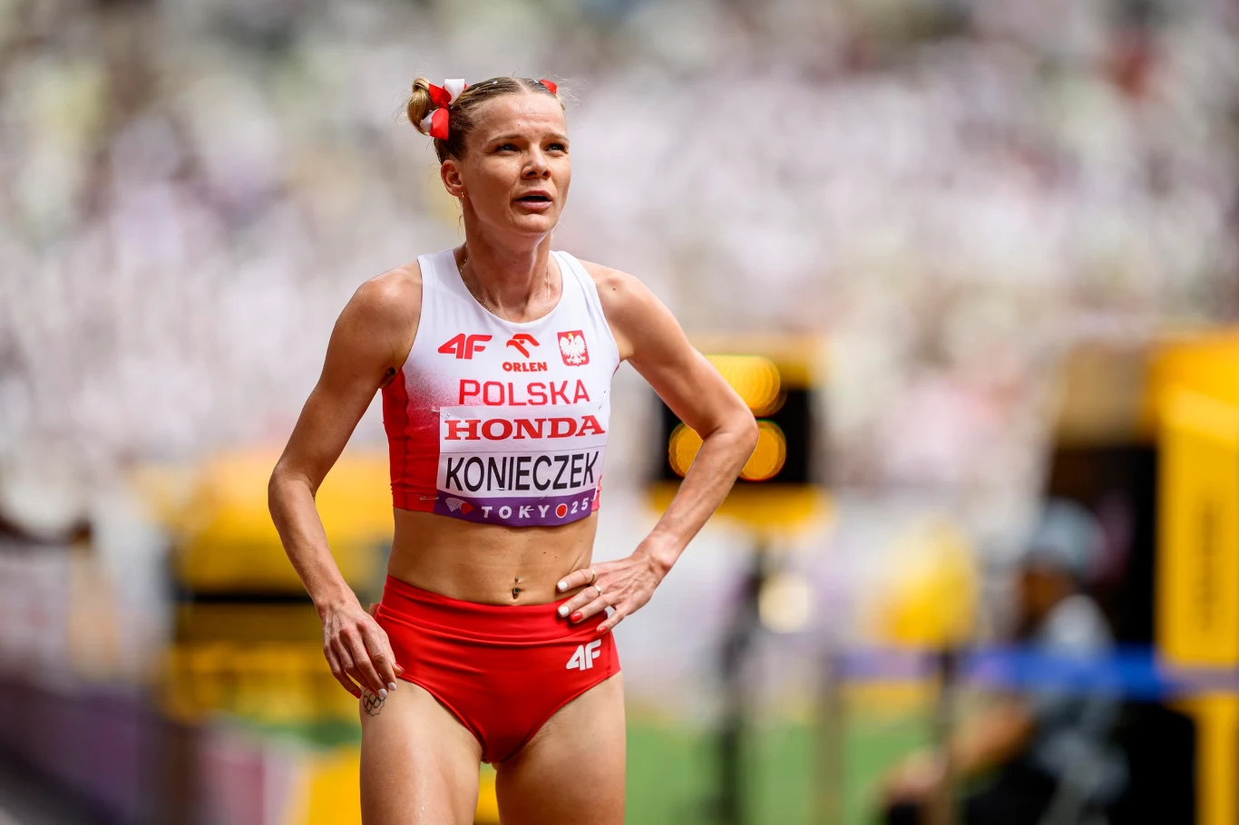 Alicja Konieczek Zawodniczka lekkoatletyczna w stroju reprezentacji Polski na tle stadionu, nosząca numer startowy z widocznym nazwiskiem i sponsorami, wyraża skupienie i zmęczenie po biegu.