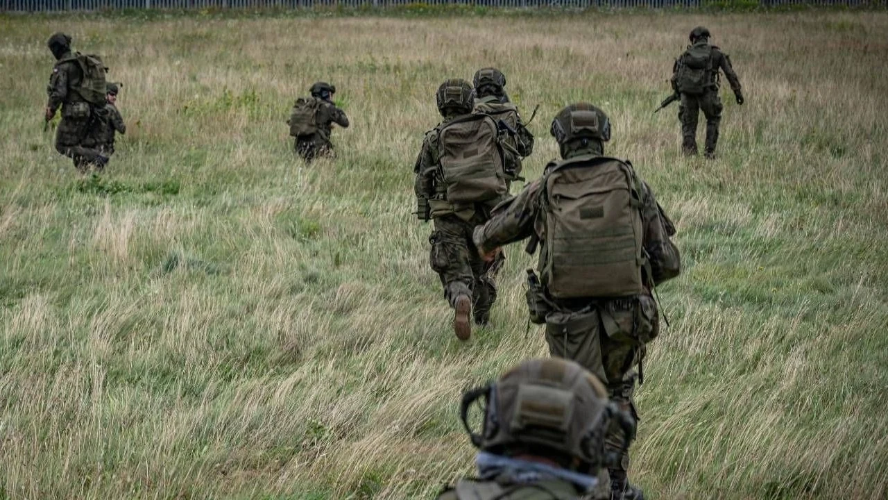Białoruskie władze krytycznie o działaniach Warszawy Grupa żołnierzy ubranych w pełne umundurowanie polowe oraz plecaki biegnie przez otwartą, trawiastą przestrzeń w kierunku niewidocznego celu, otoczenie sugeruje realizację ćwiczeń wojskowych na terenie szkoleniowym.