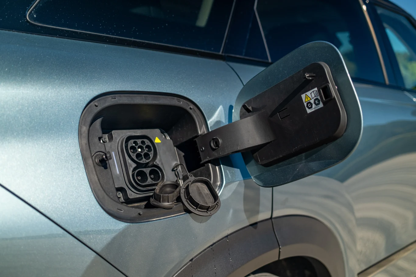 Zbliżenie na port ładowania samochodu elektrycznego znajdującego się z boku srebrnego pojazdu, z otwartą klapką i widocznymi złączami do ładowania