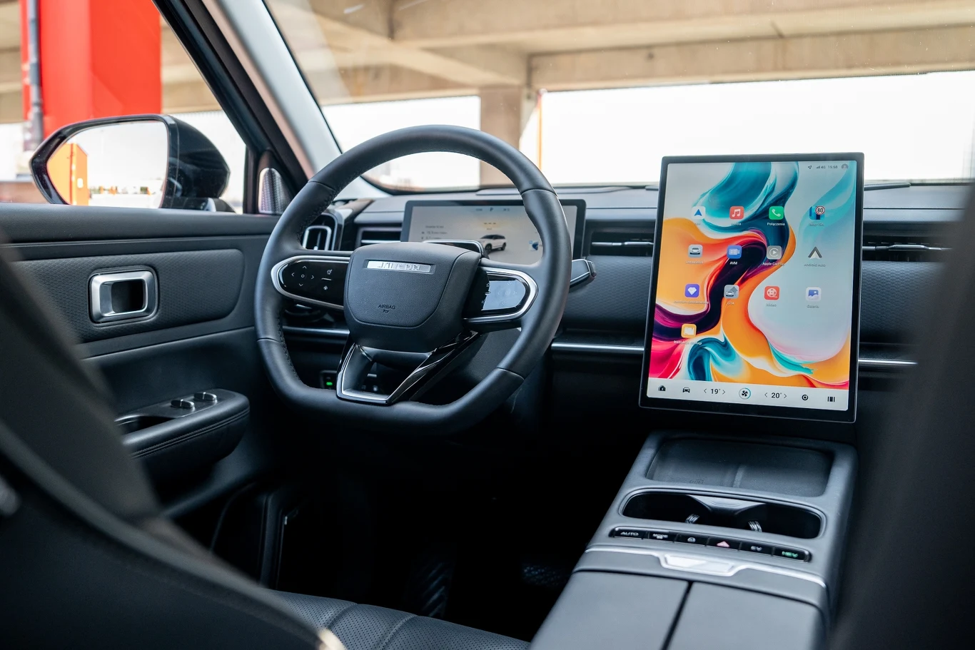 Luksusowe wnętrze samochodu z nowoczesną deską rozdzielczą, dużym ekranem dotykowym na konsoli centralnej, skórzaną kierownicą i cyfrowym zestawem wskaźników.