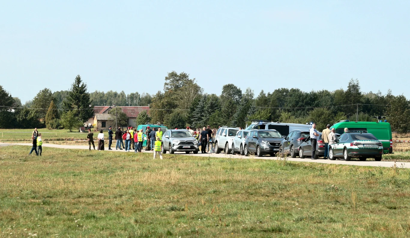 W pobliżu miejscowości Mniszków spadł jeden z rosyjskich dronów Grupa osób stojąca przy kilku samochodach zaparkowanych na bocznej drodze w otwartym terenie, wokół widoczna zielona łąka oraz pojedyncze budynki i drzewa w oddali.