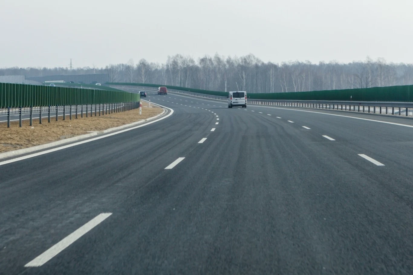 Autostrada A2 między węzłami Poznań Krzesiny i Poznań Wschód będzie dostępna z trzema pasami ruchu. Pusta, szeroka droga ekspresowa z kilkoma pojazdami, po obu stronach ekrany dźwiękochłonne i barierki, w tle rząd drzew liściastych.