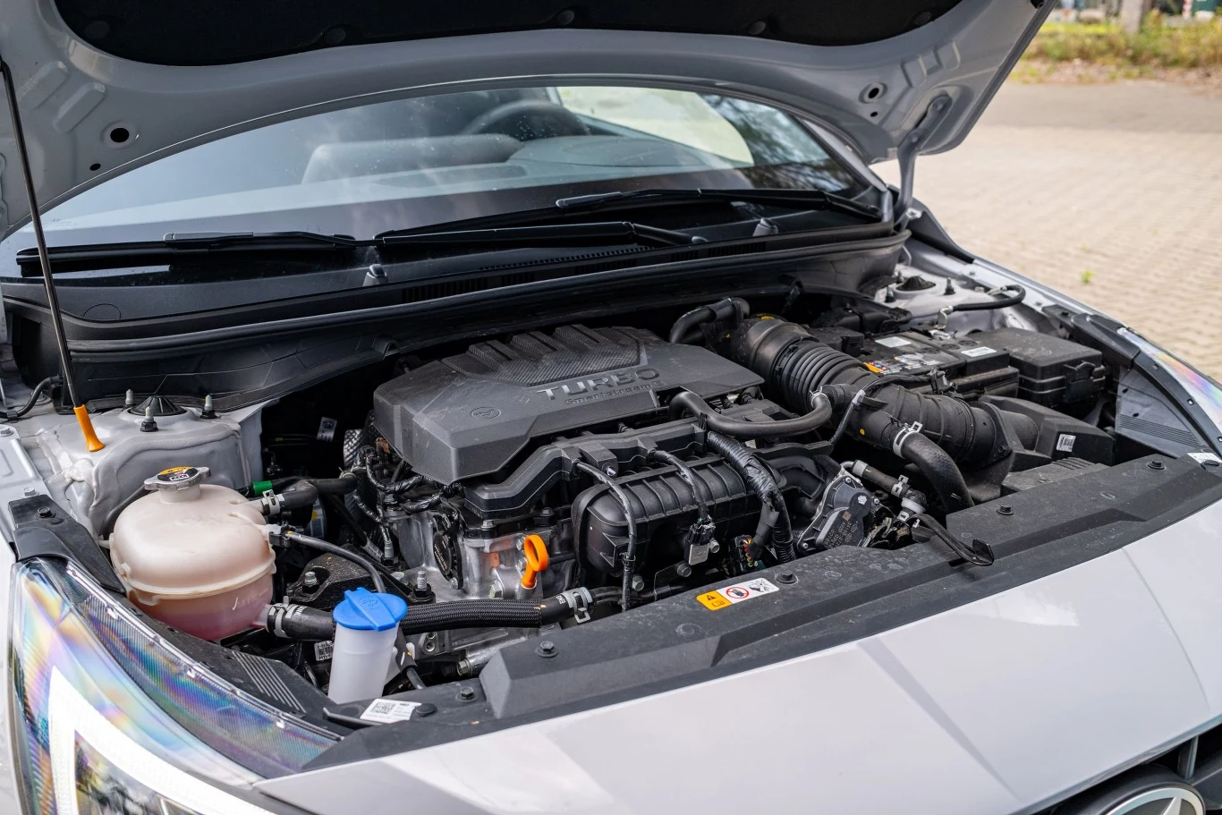 Silnik samochodowy marki Hyundai z wieloma widocznymi podzespołami mechanicznymi i płynami eksploatacyjnymi pod otwartą maską auta, otoczenie neutralne bez osób i zbędnych elementów.