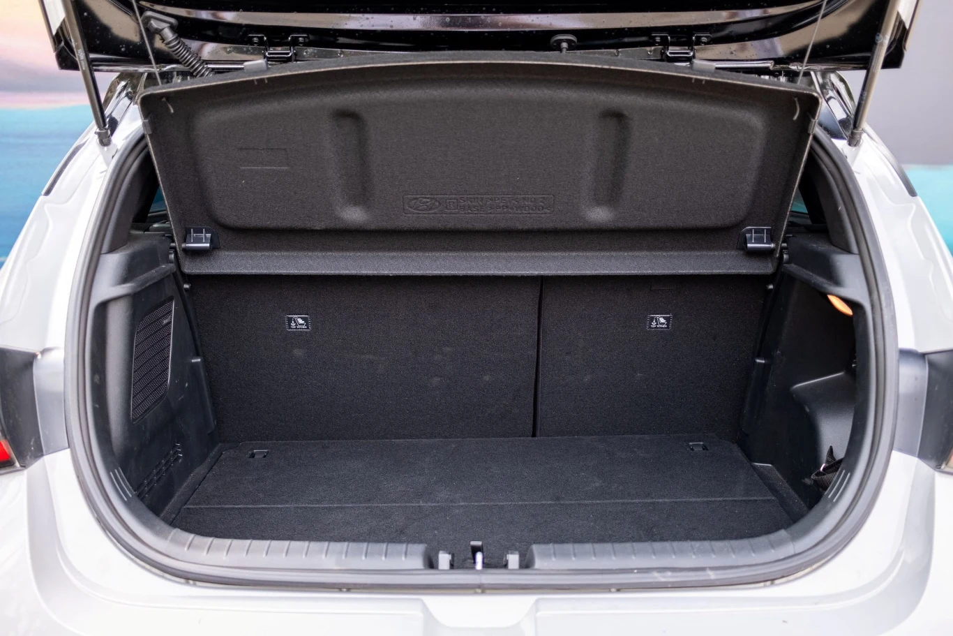 Otwarty bagażnik samochodu osobowego z unoszoną do góry klapą, wnętrze przestronne, czyste i puste, ściany boczne wykończone ciemnym materiałem, widoczna linia podziału tylnej kanapy.