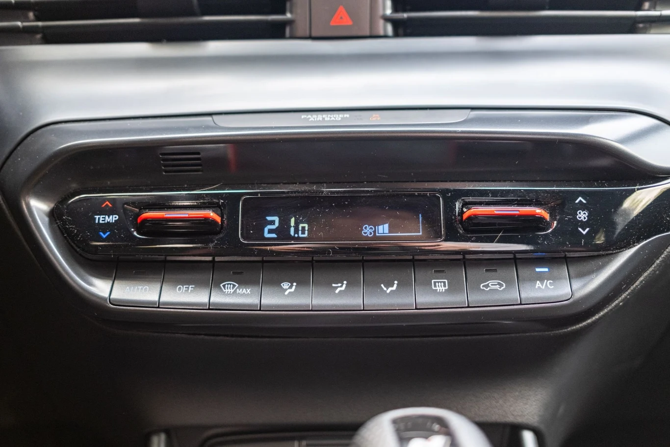 Panel sterowania klimatyzacją samochodową z cyfrowym wyświetlaczem pokazującym temperaturę 21°C, przyciskami regulacji temperatury oraz ikonami sterowania nawiewem, trybem ac i obiegiem powietrza.