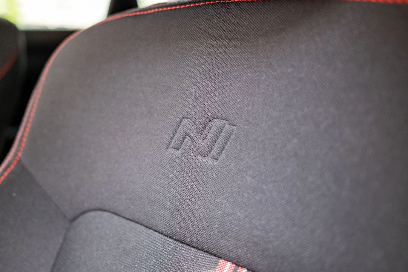 Tapicerka samochodowego fotela ze znakowaniem 'N', przeszycia czerwoną nicią na obrzeżu materiału, minimalistyczny i sportowy styl wnętrza auta.