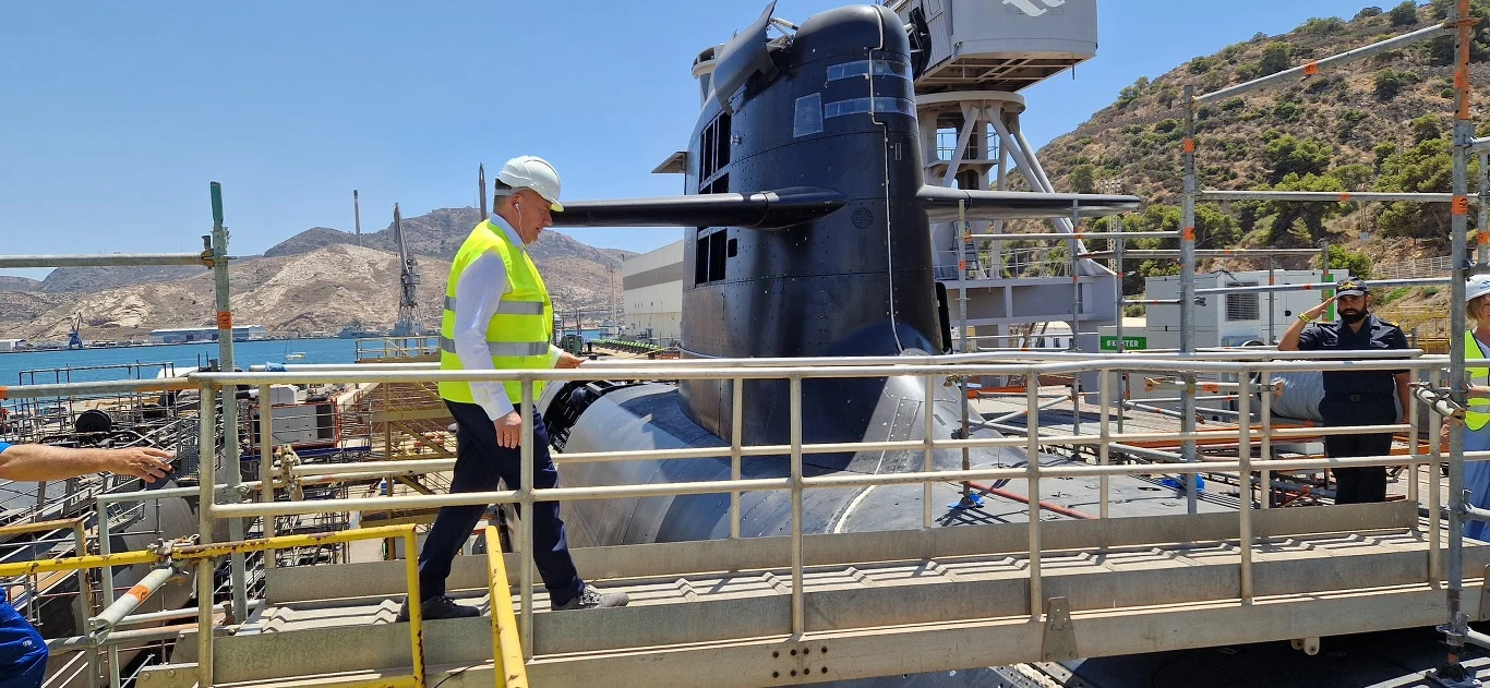 Wiceminister obrony narodowej Paweł Bejda podczas wizyty w stoczni Navantia w Kartagenie Pracownik techniczny w kamizelce odblaskowej i kasku znajduje się na podeście przy okręcie podwodnym zadokowanym w stoczni, na drugim planie widoczne są stalowe konstrukcje i wzniesienia.
