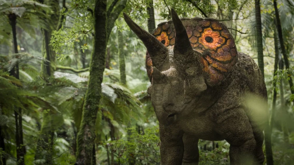 Triceratops poruszający się w gęstym, zielonym lesie tropikalnym, otoczony bujną roślinnością i paprociami, w tle wilgotne drzewa oraz miękkie światło przedzierające się przez liście