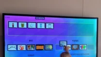 Dziewczynka dotyka dużego ekranu interaktywnego, na którym znajduje się gra edukacyjna dotycząca segregacji odpadów na różne kategorie takie jak papier, bio, szkło i tworzywa sztuczne.