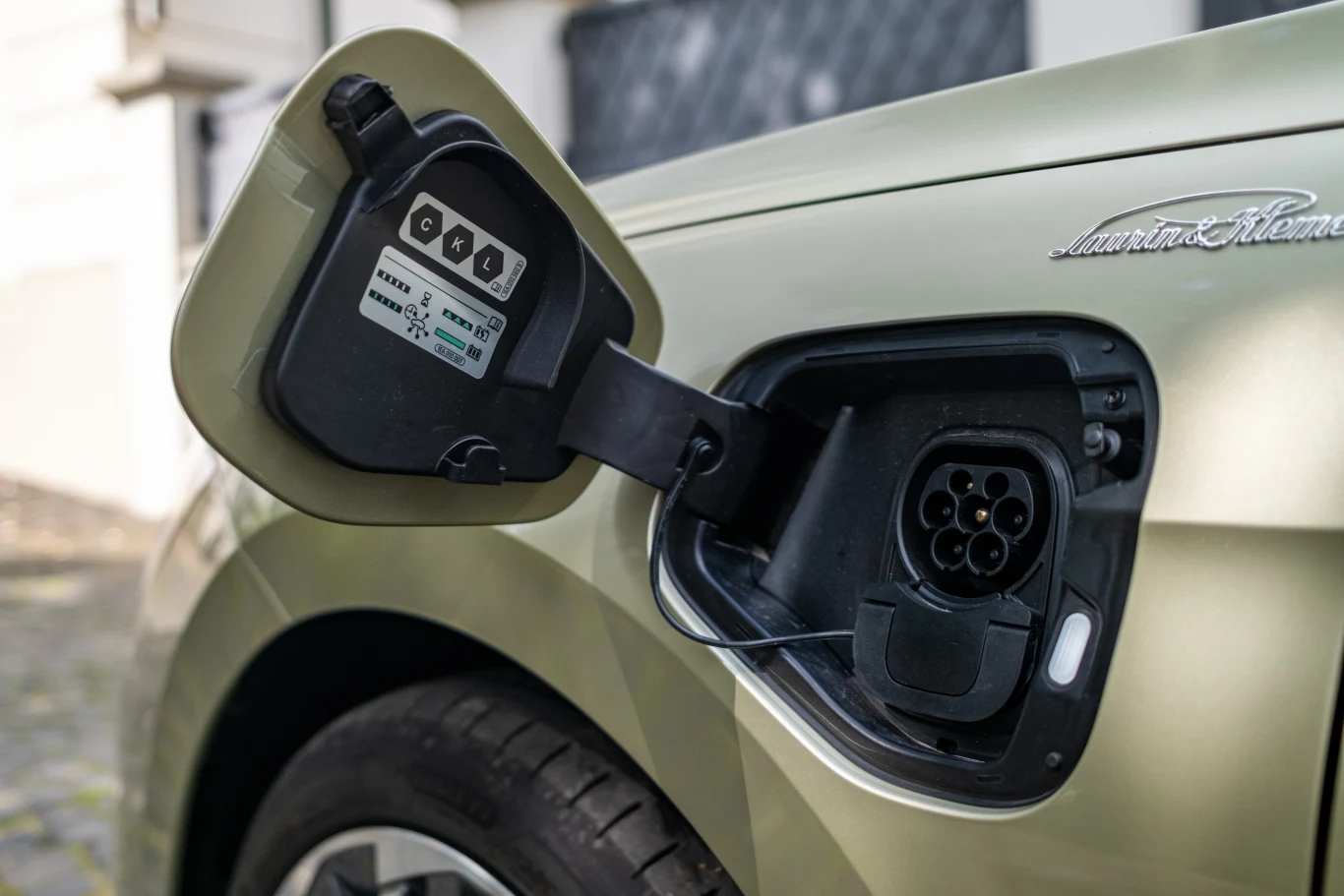 wtyczka gniazda ładowania samochodu elektrycznego oraz otwarta klapka na nadwoziu jasnozielonego pojazdu