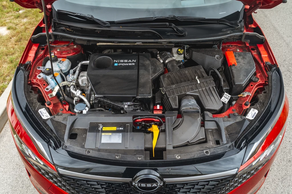 Napęd e-Power składa się z silnika spalinowego, który ładuje akumulator i silnika elektrycznego napędzającego koła Komora silnika samochodu Nissan z widocznym układem e-POWER, akumulatorem i komponentami mechanicznymi, utrzymana w czystości i dobrym stanie technicznym, sfotografowana od góry przy otwartej masce.