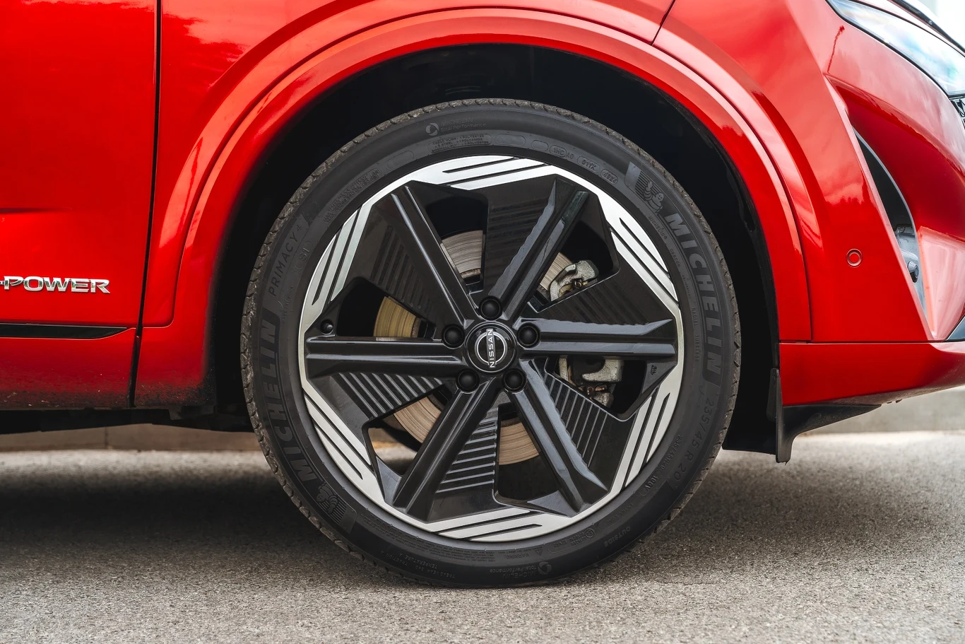 Czerwony błotnik samochodu oraz duże koło z nowoczesną felgą aluminiową i oponą Michelin na tle asfaltowej nawierzchni.