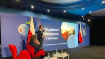 Konferencja dotycząca niezależności energetycznej i paliwowej, uczestnicy siedzą na czerwonych fotelach przed sceną z dużym ekranem, na którym widnieje prezentacja i flagi Polski oraz Unii Europejskiej.