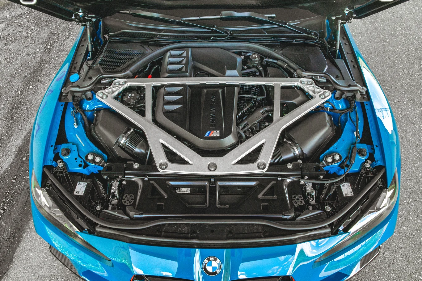 Silnik samochodowy BMW M z widocznymi elementami konstrukcyjnymi, metalowym wzmocnieniem i szczegółami technicznymi pod otwartą maską auta sportowego w kolorze niebieskim.