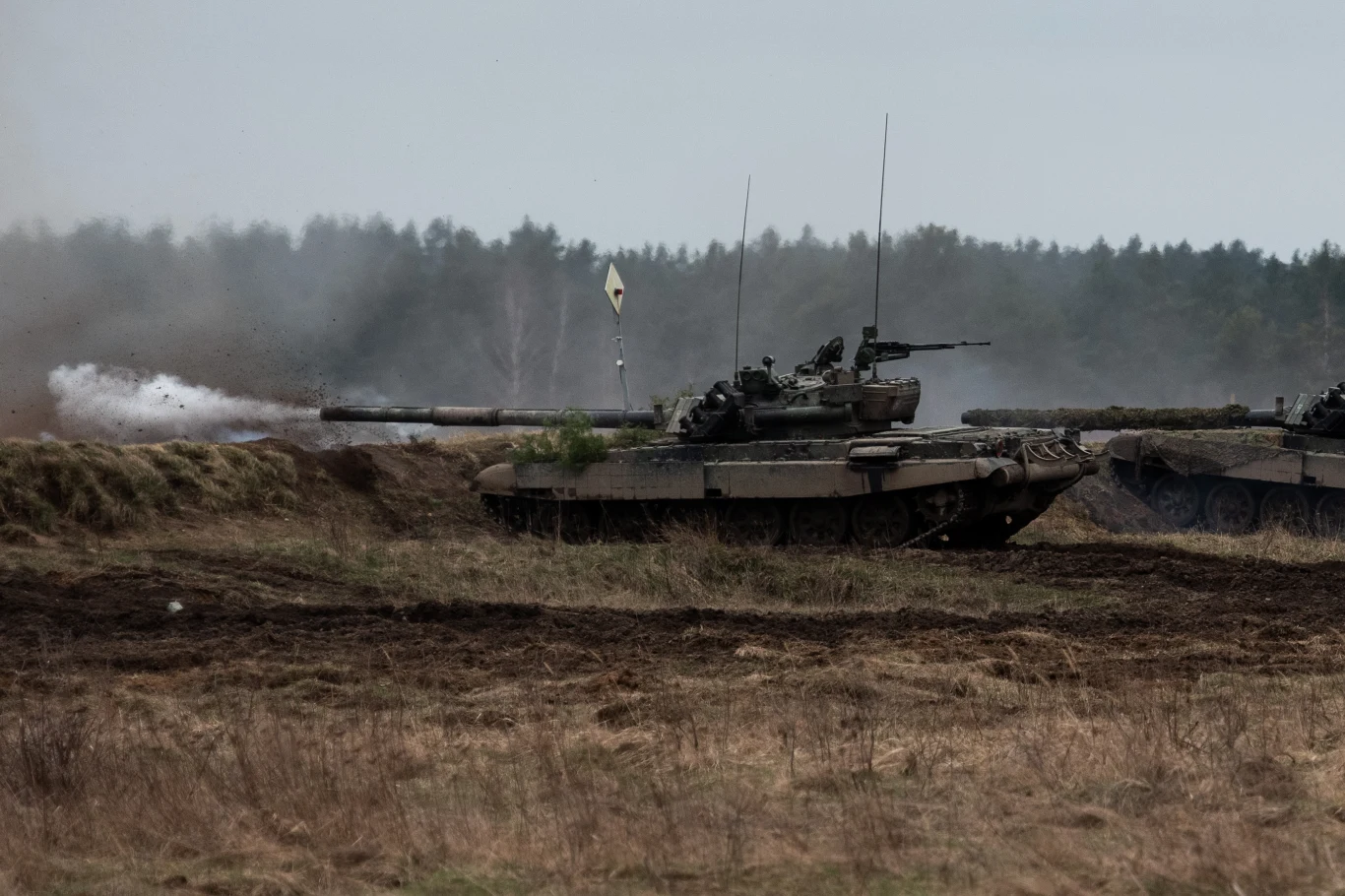 Sondaż. Co zrobią Polacy, jeśli Rosja nas napadnie? (zdj. ilustracyjne) Czołg w trakcie ćwiczeń wojskowych na otwartym, polnym terenie, widoczny dym z lufy, w tle zalesienie i neutralne niebo.