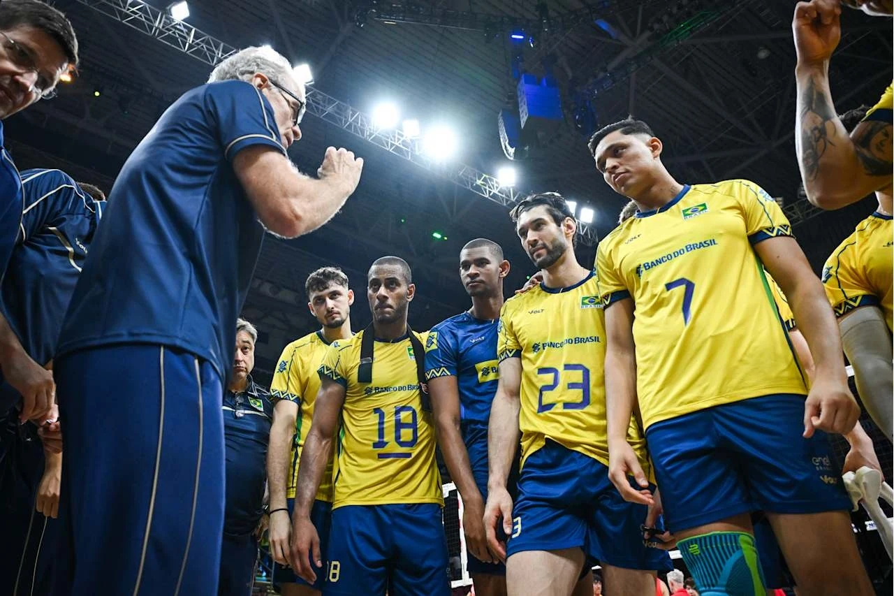 Bernardo Rezende wraz z reprezentantami Brazylii podczas MŚ na Filipinach Grupa siatkarzy w żółto-niebieskich strojach zgromadzona wokół trenera podczas intensywnej rozmowy. Zawodnicy skupieni, słuchający uwag w trakcie przerwy meczowej, wyraźne napięcie i koncentracja. W tle elementy hali sportowej i oświetlenie.