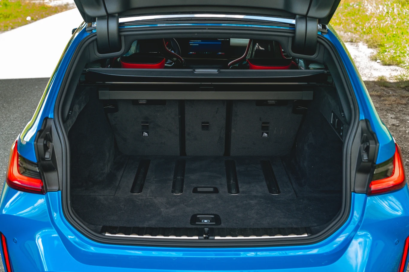 Otwarty bagażnik niebieskiego samochodu osobowego z dużą przestrzenią ładunkową, wyłożony czarną tapicerką i widocznymi składanymi oparciami tylnych siedzeń.