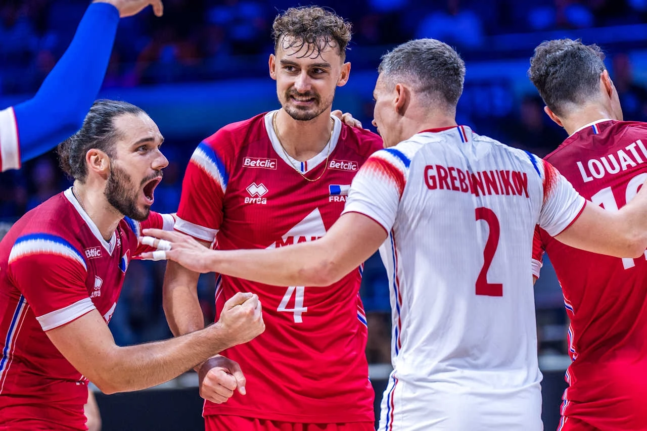 Siatkarze reprezentacji Francji Zawodnicy drużyny siatkarskiej ubrani w czerwono-białe stroje celebrują wspólnie punkt zdobyty podczas meczu, widoczne emocje i radość na twarzach sportowców, w tle rozmazana publiczność.
