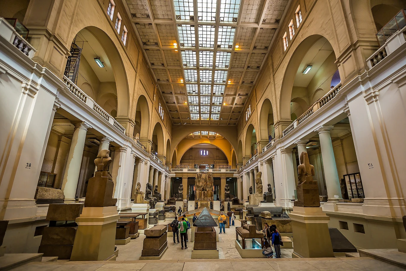 Wnętrze dużego muzeum z wysokimi, sklepionymi sufitami, licznymi kolumnami oraz ekspozycją monumentalnych rzeźb i artefaktów starożytnego Egiptu, pośród których spacerują zwiedzający.