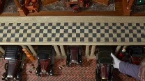 Kilka modeli zabytkowych samochodów ustawionych w rzędzie w miniaturowym garażu, przedzielonych kolumnami, na pierwszym planie widoczne dłonie osoby w białych rękawiczkach manipulującej jednym z autek, posadzka ozdobiona wzorem w kratę.