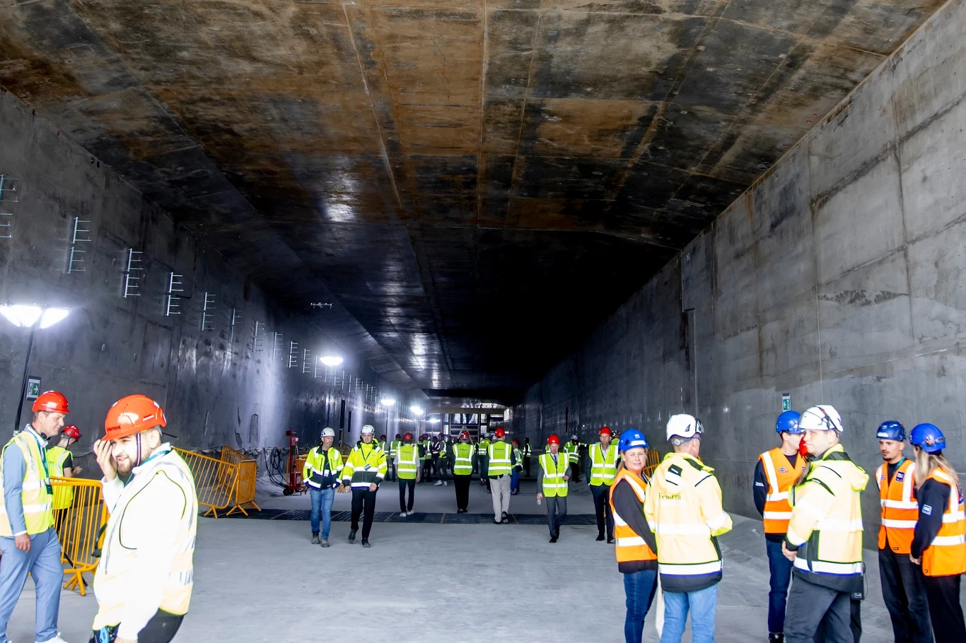 Budowa tunelu pod Bełtem Fehmarn. Tak wygląda pojedynczy element o wadze 73 tys. ton Ludzie w kamizelkach odblaskowych i kaskach ochronnych podczas inspekcji lub pracy w szerokim, oświetlonym tunelu budowlanym o betonowych ścianach i suficie.
