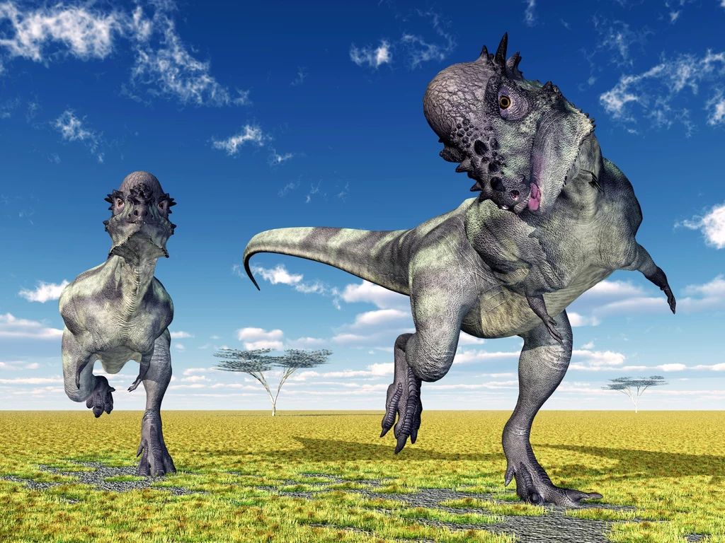 Dwa dinozaury biegające po trawiastej, suchej równinie pod niebieskim niebem z kilkoma drzewami w tle; realistyczna ilustracja prehistorycznej sceny.
