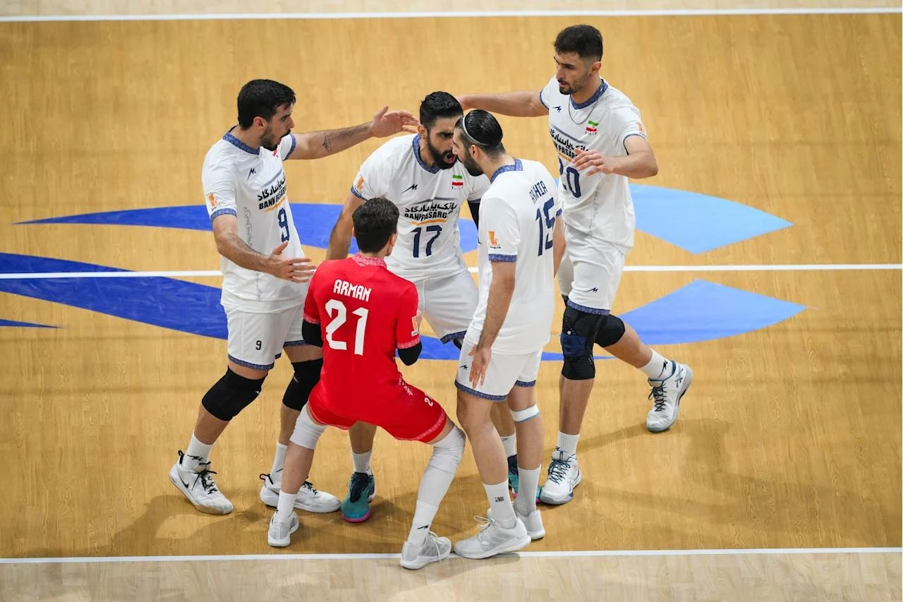 Siatkarze reprezentacji Iranu Grupa siatkarzy ubranych w białe i czerwone stroje świętuje wspólnie na parkiecie hali sportowej, wyrażając radość i podnosząc dłonie do góry.