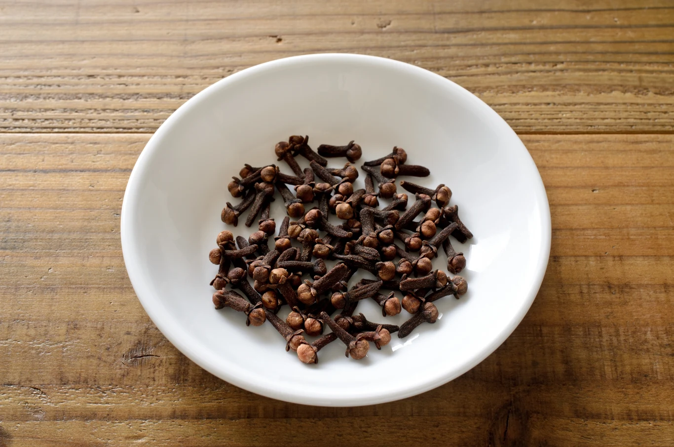 Biała miseczka z suszonymi goździkami ustawiona na drewnianym blacie